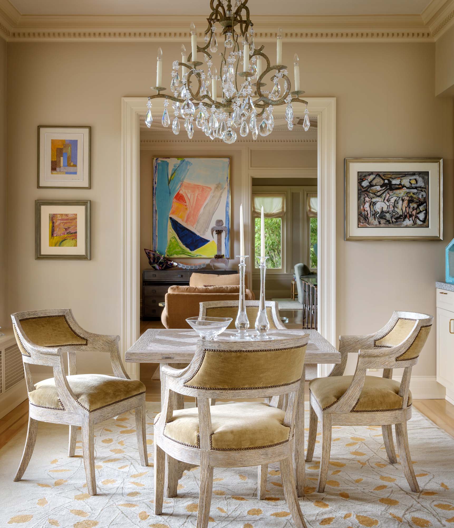table for four with candlesticks, chandelier above, cushioned chairs around, and artwork on the walls